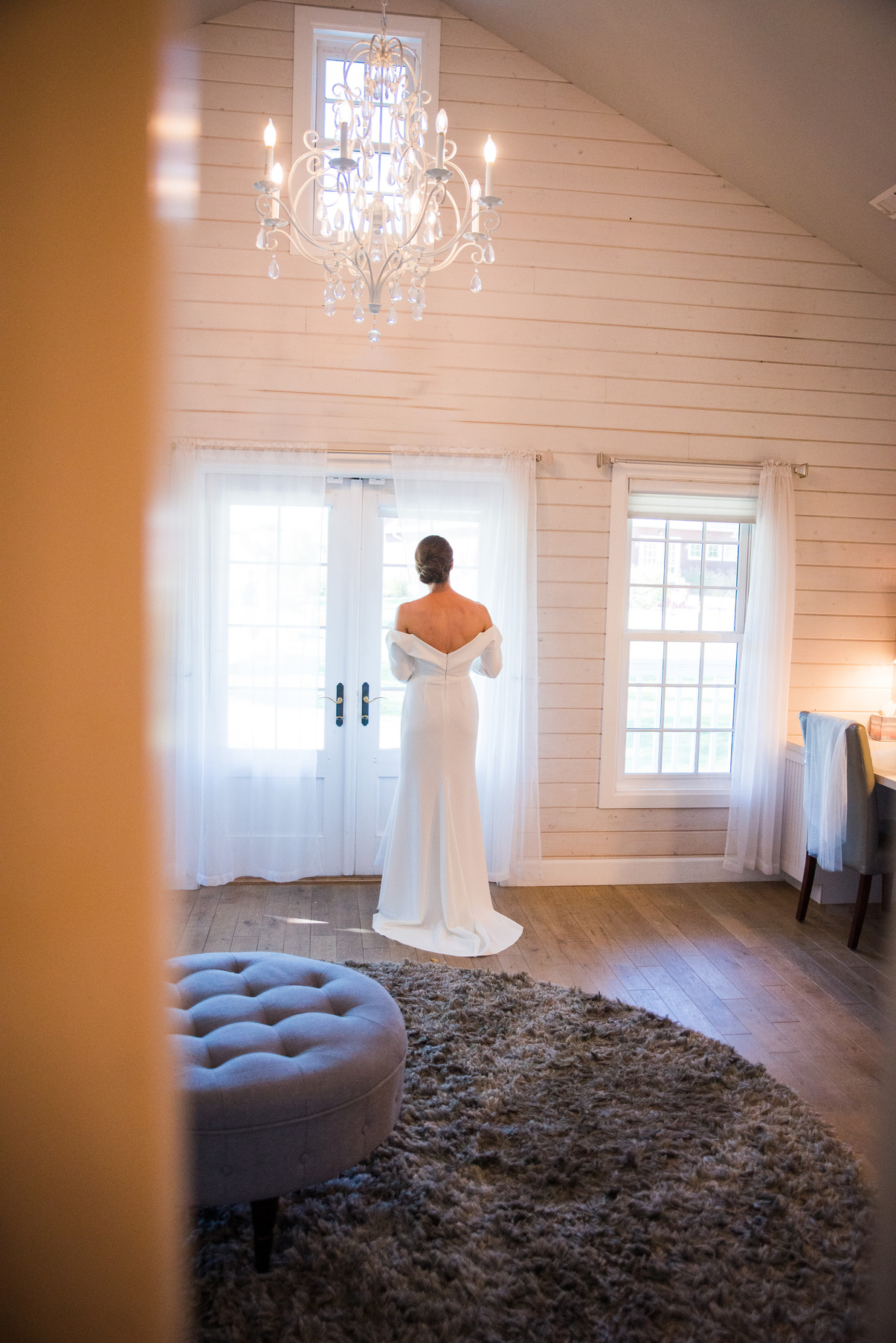 A bride in a wedding dress standing in front of a window in the getting ready space at The Barn at Raccoon Creek in Littleton, Colorado