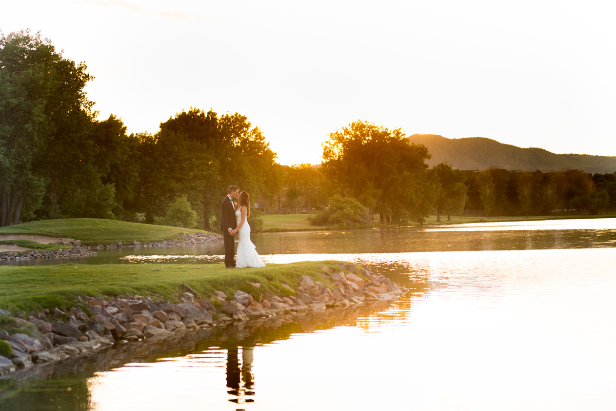 A wide-angle shot of a bride and groom standing next to the lake at The Barn at Raccoon Creek during Colorado golden hour.