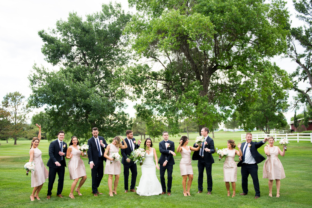 A wedding party playfully makes silly poses for the camera while the couple stands in the center.