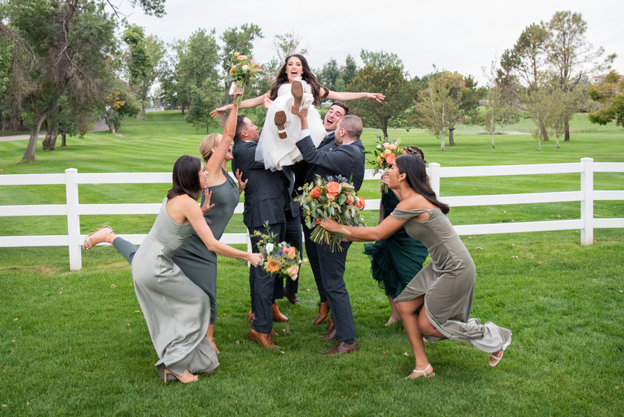 A group of bridesmaids and groomsmen playfully toss the bride in the air.