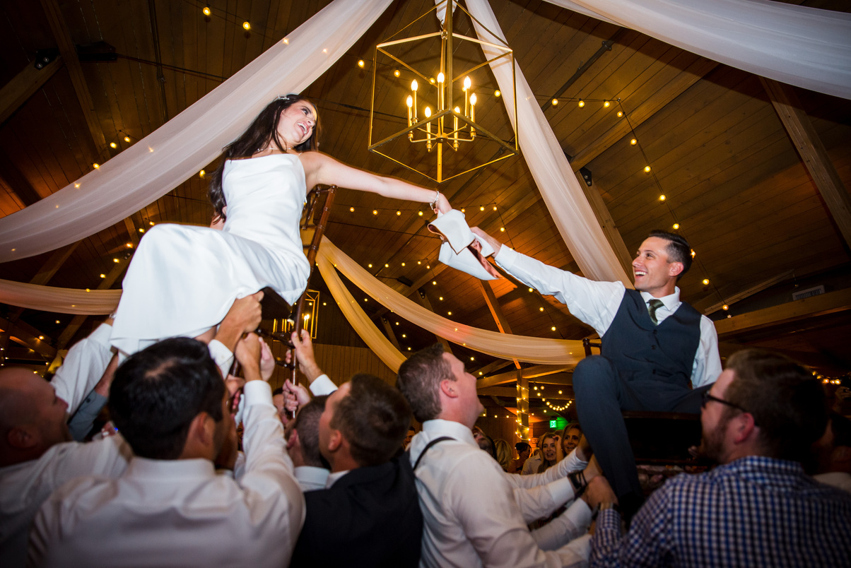A bride and groom are lifted into the air by their friends at a wedding reception at The Barn at Raccoon Creek in Littleton, Colorado.