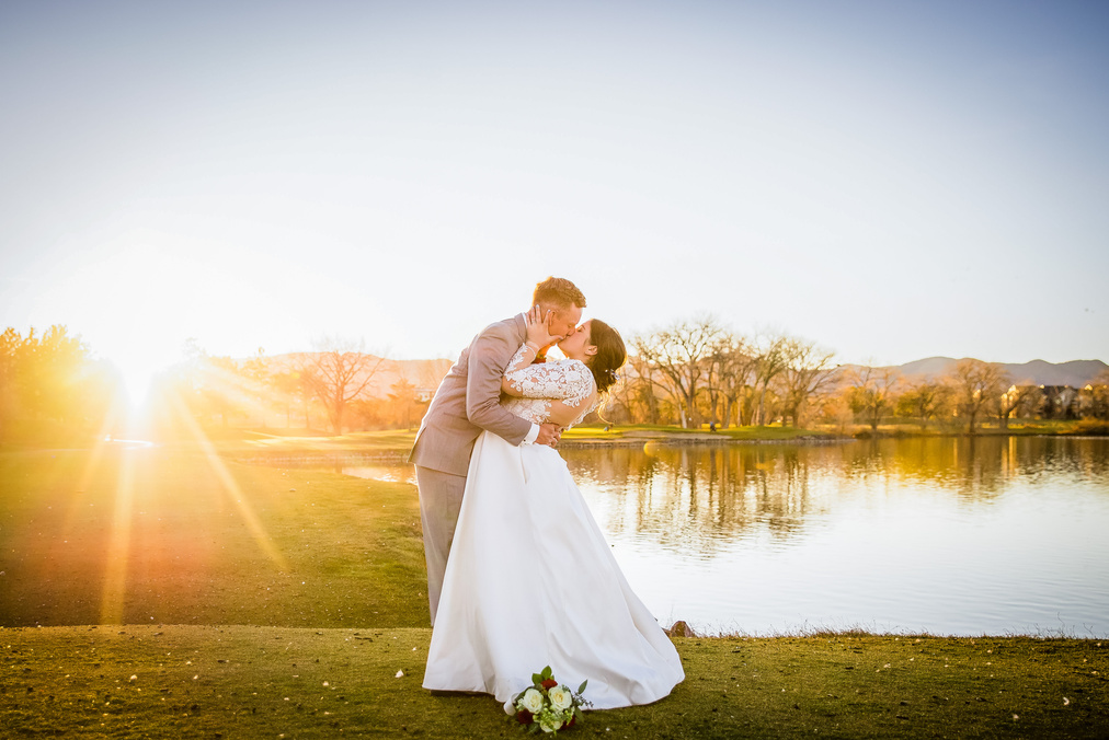 A groom dips his bride for a kiss as she grabs his face in front of the lake at sunset at The Barn at Raccoon Creek.