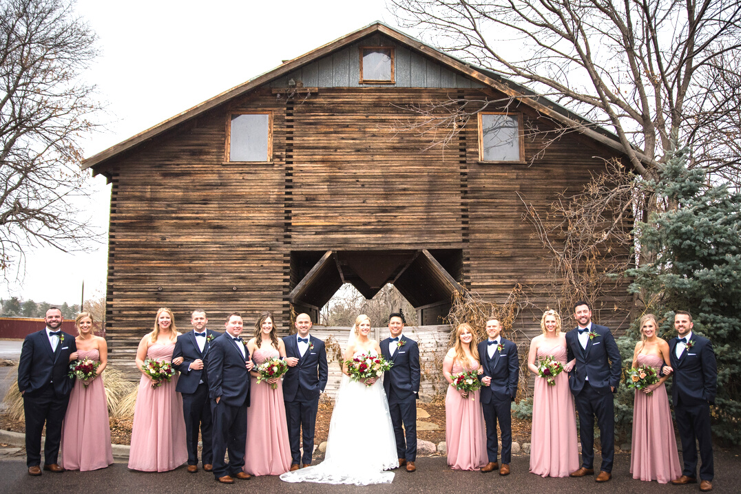 A group of bridesmaids and groomsmen standing in front of a rustic barn at The Barn At Raccoon Creek in Littleton, Colorado.