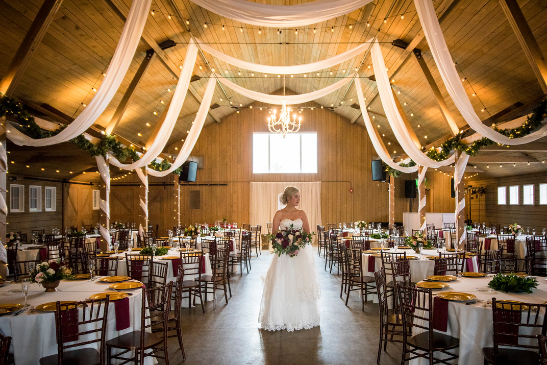 A bride standing in the middle of a barn with white drapes hanging from the ceiling.