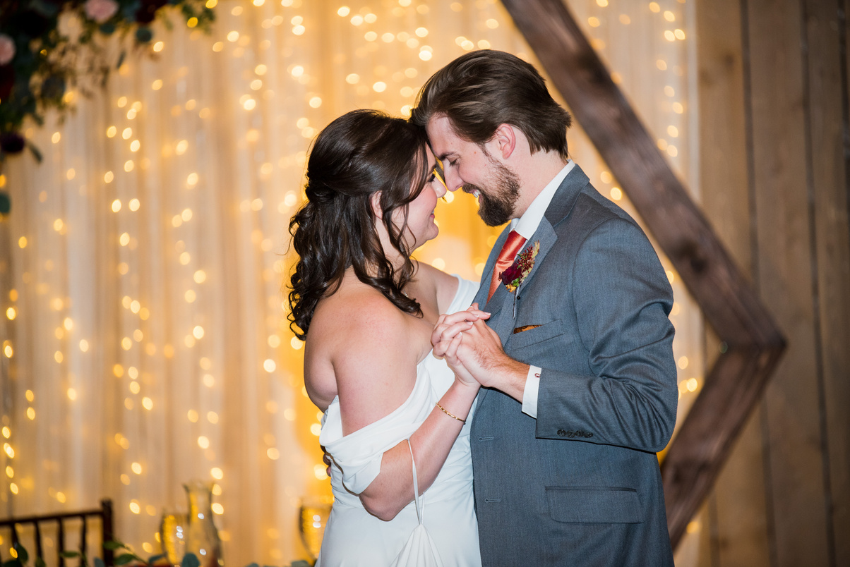 A bride and groom share their first dance with twinkle lights in the background.